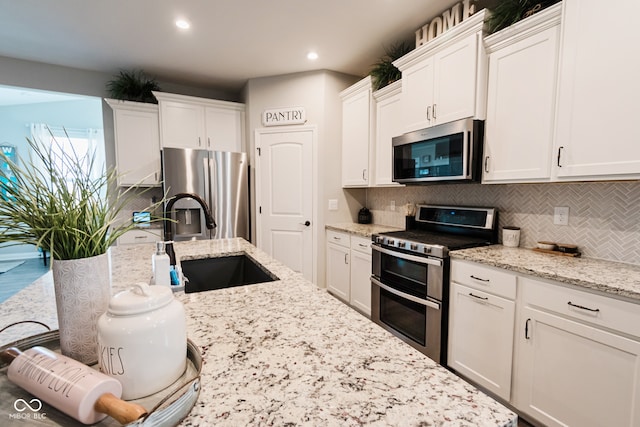 kitchen featuring decorative backsplash, sink, white cabinetry, appliances with stainless steel finishes, and light stone counters