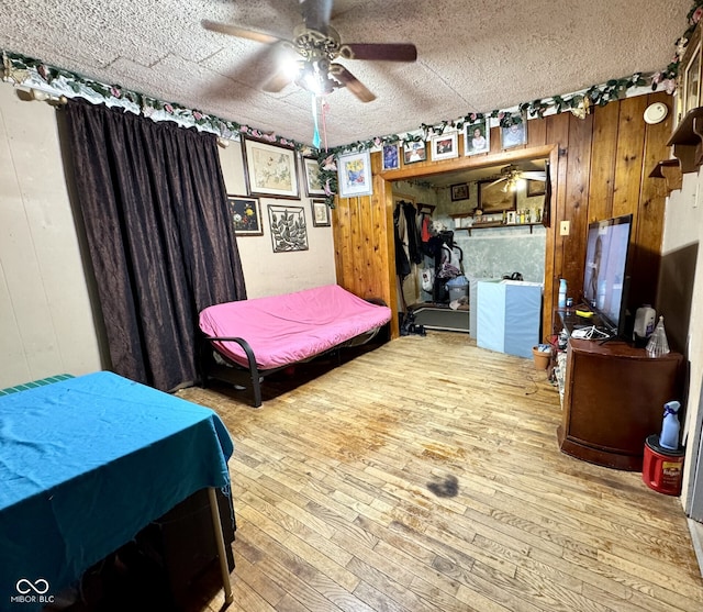 bedroom featuring hardwood / wood-style flooring, ceiling fan, a textured ceiling, and wooden walls