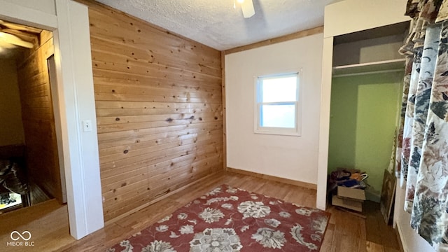 bedroom with hardwood / wood-style floors, wooden walls, a textured ceiling, and ceiling fan