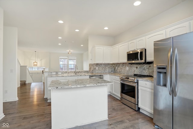 kitchen featuring kitchen peninsula, hardwood / wood-style flooring, stainless steel appliances, sink, and decorative light fixtures