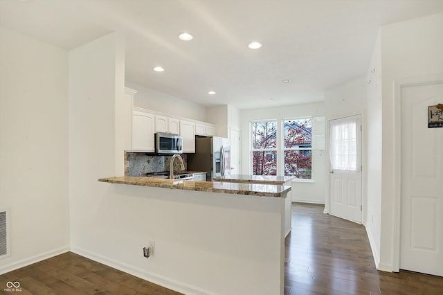 kitchen featuring kitchen peninsula, backsplash, appliances with stainless steel finishes, white cabinetry, and dark hardwood / wood-style floors