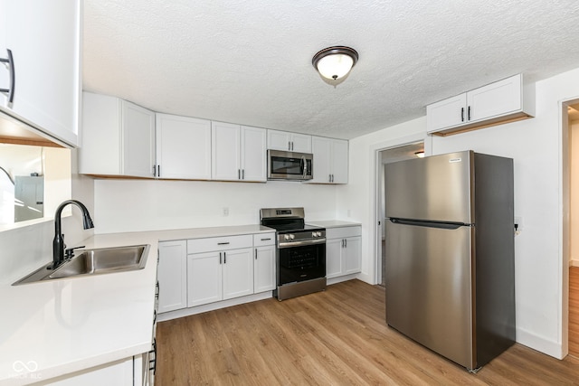 kitchen with appliances with stainless steel finishes, sink, light wood-type flooring, and white cabinets