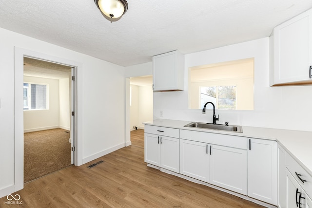 kitchen featuring white cabinetry, light hardwood / wood-style floors, a textured ceiling, and sink