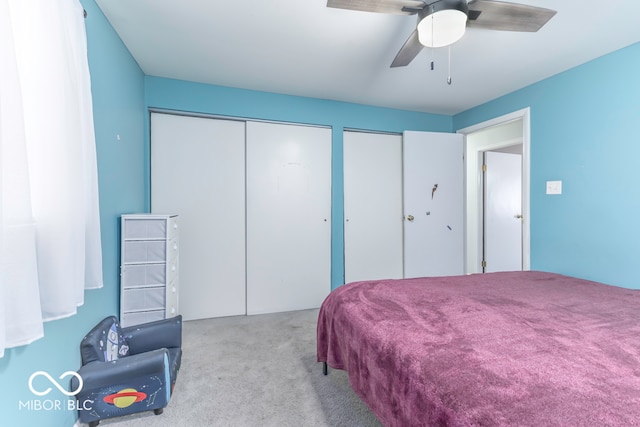 bedroom featuring ceiling fan, light carpet, and multiple closets