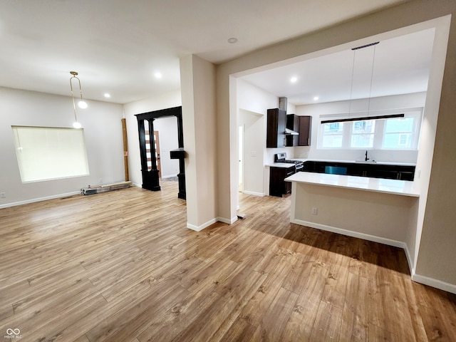 kitchen with hanging light fixtures, sink, dark brown cabinets, and light wood-type flooring