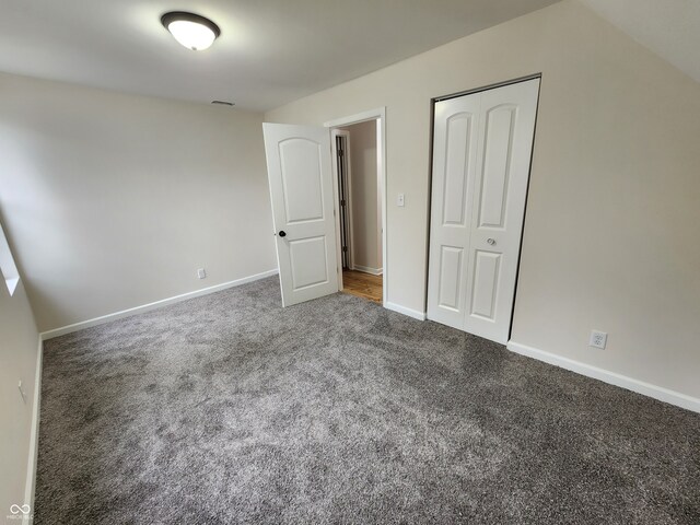 unfurnished bedroom with dark colored carpet and a closet