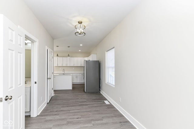 hallway with light hardwood / wood-style floors, a notable chandelier, and sink