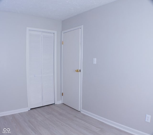 unfurnished bedroom featuring light hardwood / wood-style flooring, a textured ceiling, and a closet