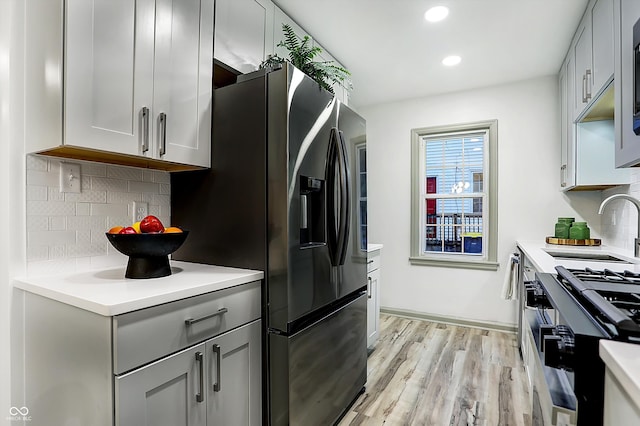 kitchen featuring stainless steel appliances, decorative backsplash, sink, gray cabinets, and light wood-type flooring