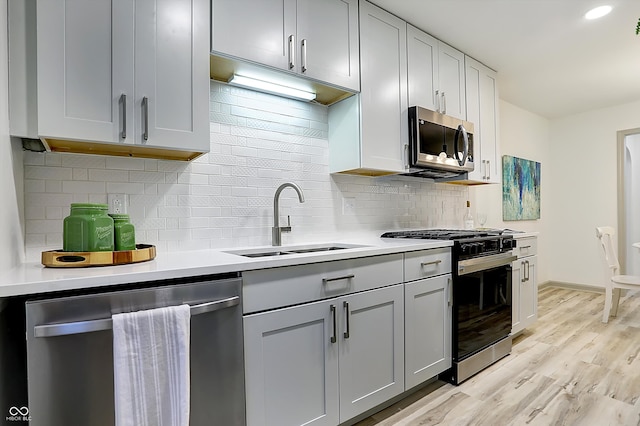 kitchen with stainless steel appliances, sink, tasteful backsplash, gray cabinetry, and light wood-type flooring