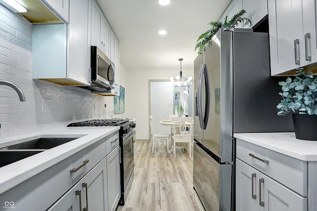 kitchen featuring light hardwood / wood-style floors, sink, appliances with stainless steel finishes, an inviting chandelier, and hanging light fixtures