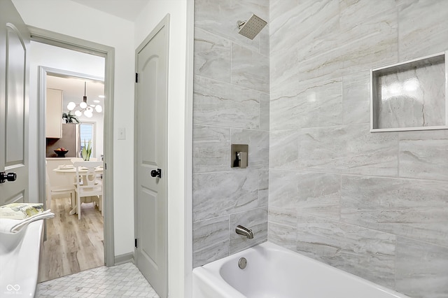 bathroom with hardwood / wood-style flooring, tiled shower / bath, and an inviting chandelier