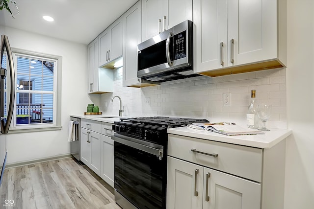 kitchen with stainless steel appliances, white cabinetry, sink, tasteful backsplash, and light hardwood / wood-style flooring