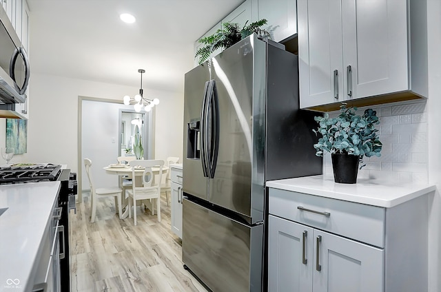 kitchen featuring stainless steel appliances, light hardwood / wood-style floors, backsplash, hanging light fixtures, and a chandelier