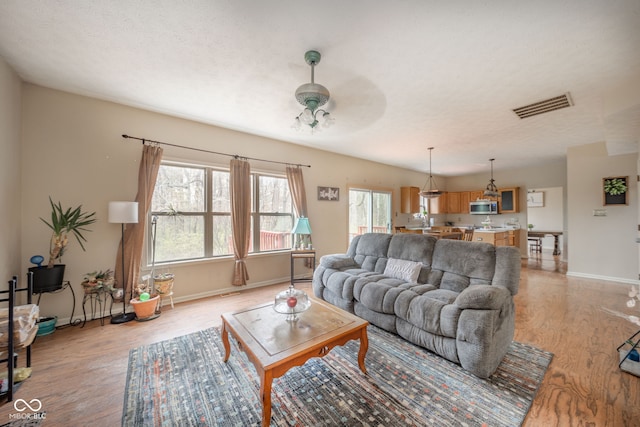 living room with light hardwood / wood-style floors, a textured ceiling, and ceiling fan