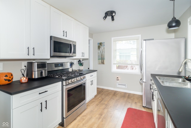 kitchen with white cabinets, appliances with stainless steel finishes, decorative light fixtures, and light hardwood / wood-style flooring