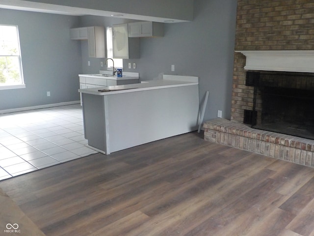 kitchen with kitchen peninsula, wood-type flooring, sink, a fireplace, and white cabinets