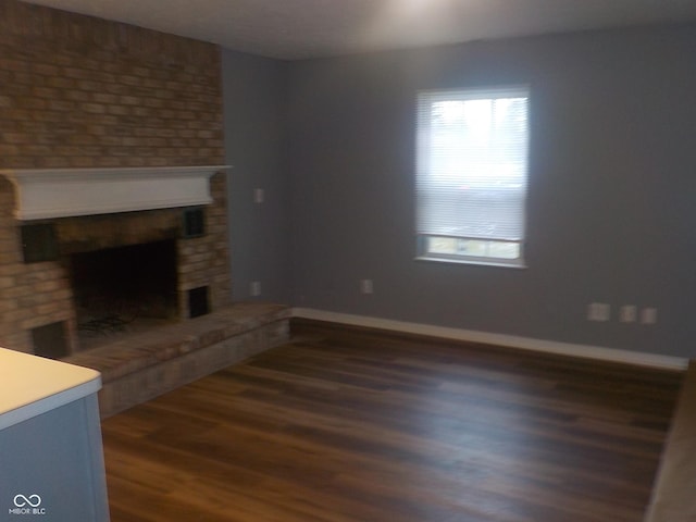 unfurnished living room with a brick fireplace and dark wood-type flooring