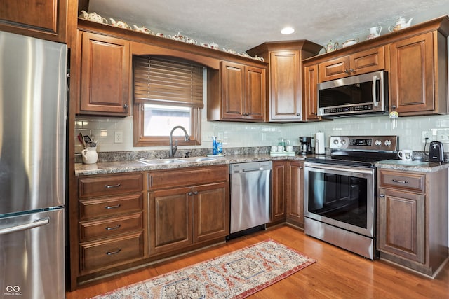 kitchen featuring tasteful backsplash, appliances with stainless steel finishes, sink, a textured ceiling, and light hardwood / wood-style floors