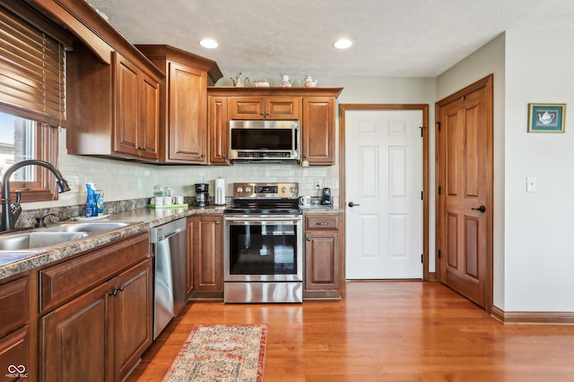 kitchen featuring backsplash, sink, appliances with stainless steel finishes, and light wood-type flooring