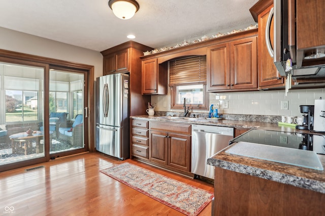 kitchen with light hardwood / wood-style floors, stainless steel appliances, sink, and backsplash