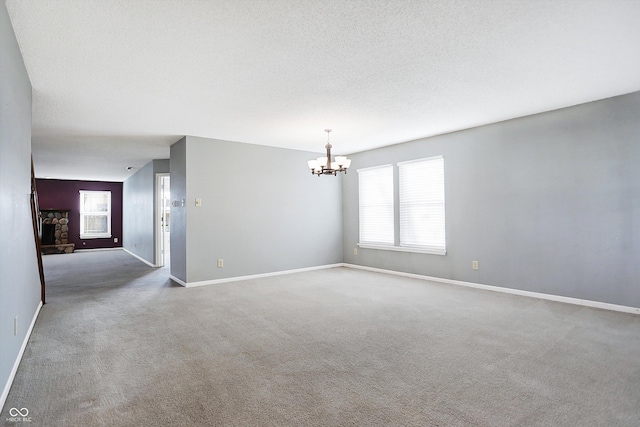 spare room with a notable chandelier, a fireplace, carpet floors, and a textured ceiling