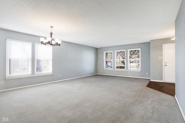 carpeted empty room featuring a chandelier and a textured ceiling