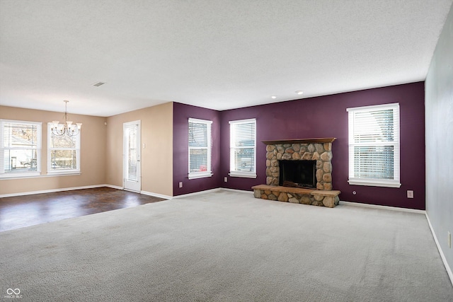 unfurnished living room featuring a stone fireplace, a wealth of natural light, a textured ceiling, and an inviting chandelier