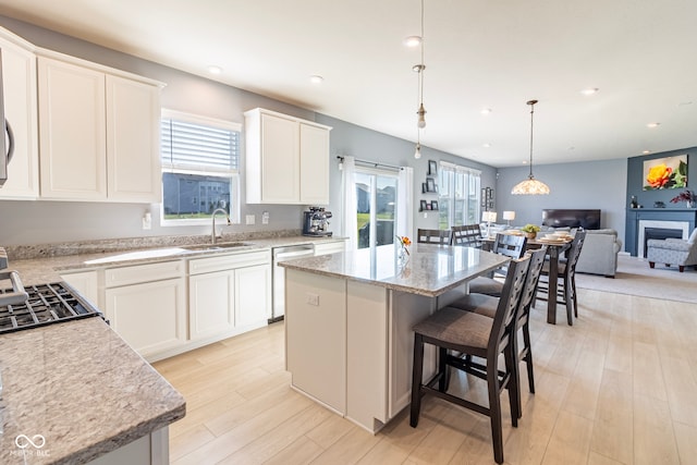 kitchen with white cabinets, appliances with stainless steel finishes, a kitchen island, sink, and hanging light fixtures