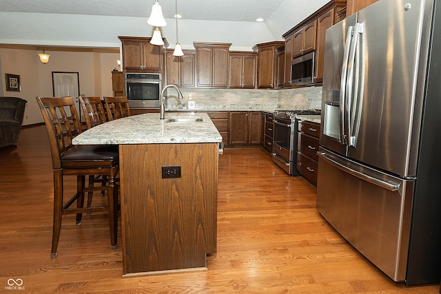 kitchen with decorative backsplash, sink, an island with sink, light wood-type flooring, and appliances with stainless steel finishes