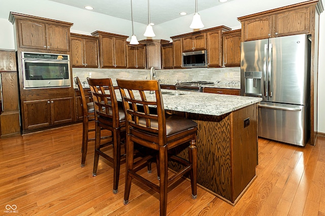 kitchen with stainless steel appliances, a kitchen island, light wood-type flooring, backsplash, and decorative light fixtures