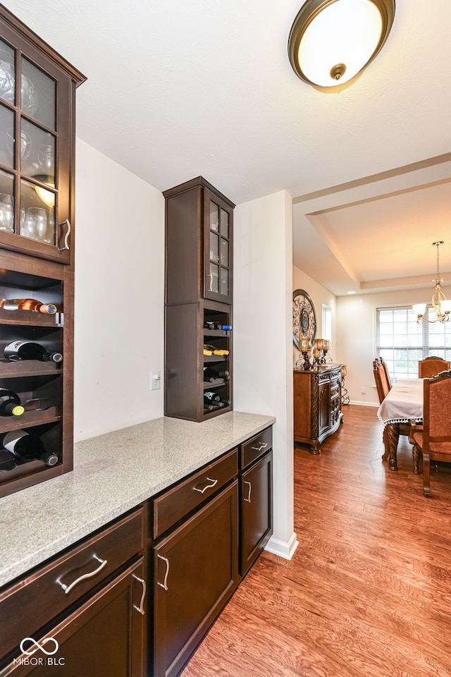 kitchen with pendant lighting, a notable chandelier, light wood-type flooring, light stone counters, and dark brown cabinets