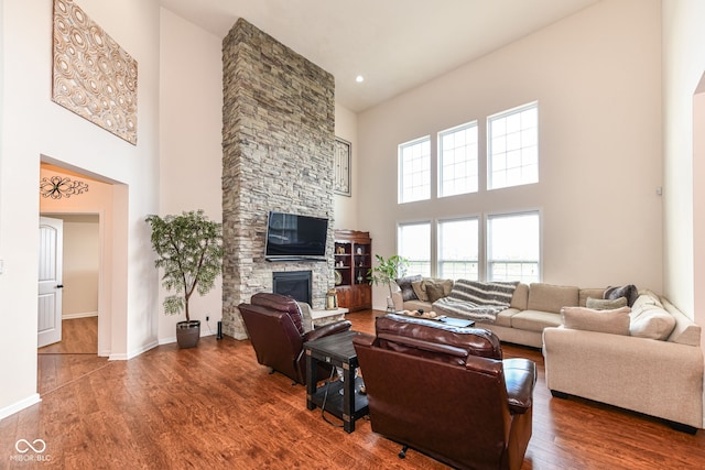 living room with a high ceiling, dark hardwood / wood-style floors, and a stone fireplace