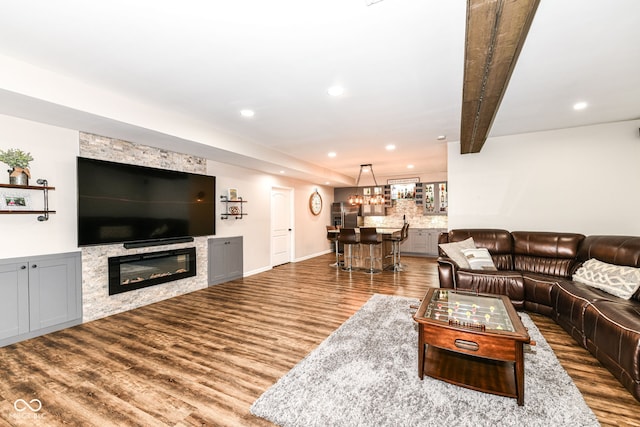 living room featuring beam ceiling, bar area, a stone fireplace, and hardwood / wood-style floors