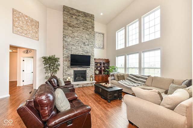 living room with a fireplace, a towering ceiling, and hardwood / wood-style flooring