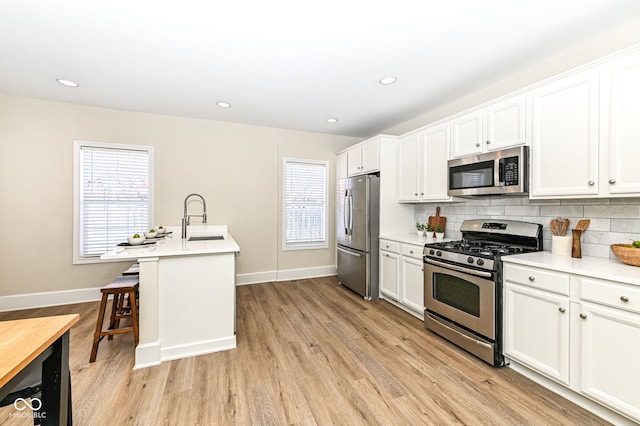 kitchen with appliances with stainless steel finishes, a kitchen breakfast bar, white cabinets, an island with sink, and tasteful backsplash