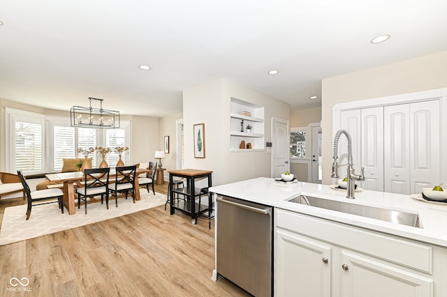 kitchen featuring sink, light wood-type flooring, dishwasher, decorative light fixtures, and white cabinets