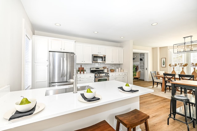 kitchen featuring light wood-type flooring, stainless steel appliances, white cabinetry, and pendant lighting