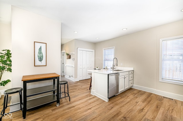 kitchen with kitchen peninsula, dishwasher, light wood-type flooring, and sink