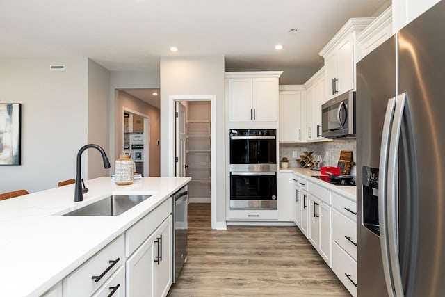 kitchen with tasteful backsplash, appliances with stainless steel finishes, sink, white cabinetry, and light hardwood / wood-style flooring