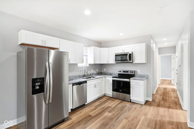 kitchen with white cabinetry, sink, light stone counters, light hardwood / wood-style flooring, and appliances with stainless steel finishes