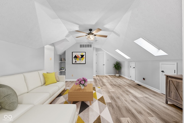 living room featuring a textured ceiling, light hardwood / wood-style flooring, ceiling fan, and vaulted ceiling with skylight