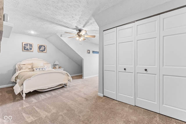 carpeted bedroom with ceiling fan, lofted ceiling, a textured ceiling, and a closet