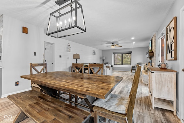 dining area featuring wood walls, ceiling fan with notable chandelier, wood-type flooring, and a textured ceiling