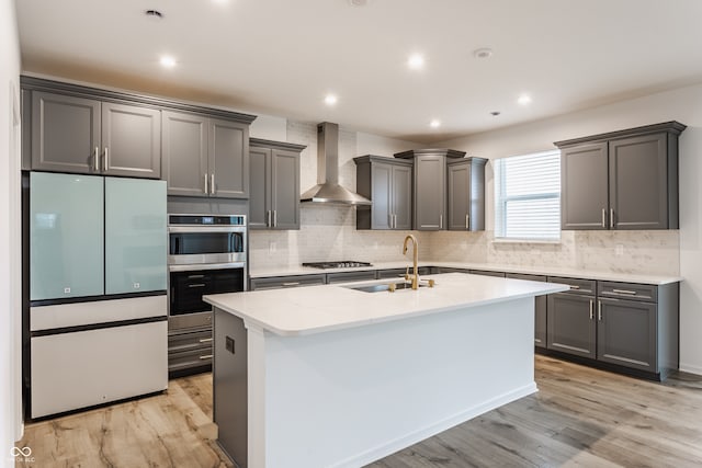 kitchen featuring light hardwood / wood-style floors, sink, wall chimney range hood, and an island with sink