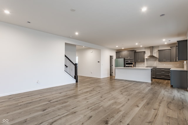 kitchen featuring gray cabinetry, wall chimney range hood, appliances with stainless steel finishes, light hardwood / wood-style floors, and a center island