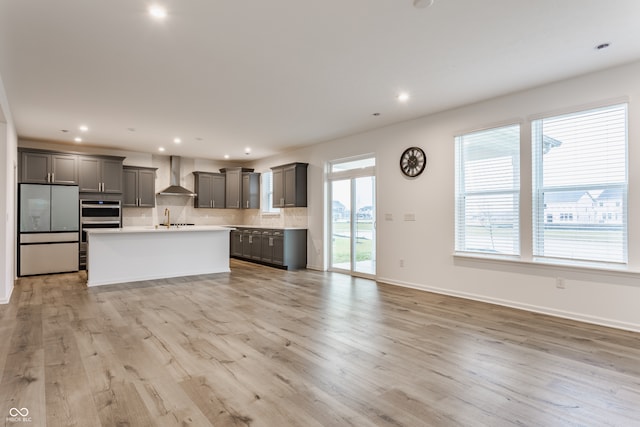 kitchen with stainless steel appliances, a wealth of natural light, wall chimney range hood, and light hardwood / wood-style flooring