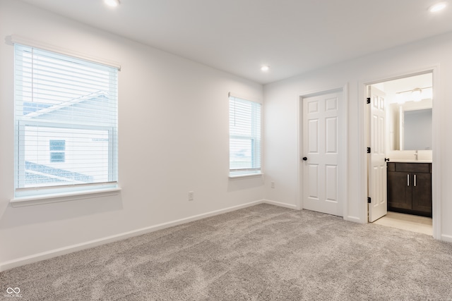 unfurnished bedroom with light colored carpet, multiple windows, and connected bathroom