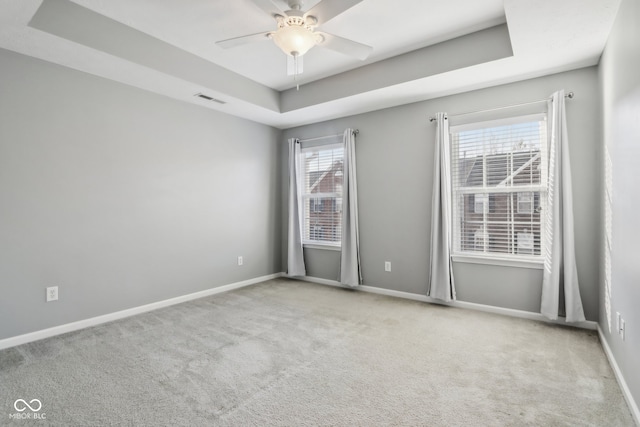 carpeted spare room with ceiling fan, a healthy amount of sunlight, and a raised ceiling