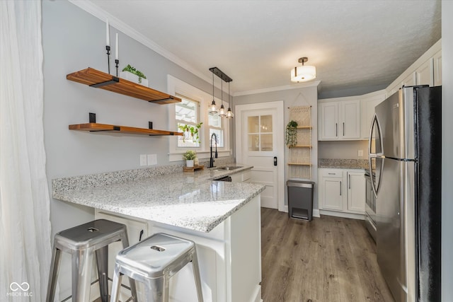 kitchen with white cabinets, sink, stainless steel fridge, kitchen peninsula, and a breakfast bar area